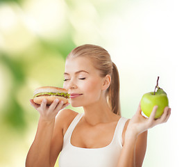 Image showing woman smelling hamburger and holding apple