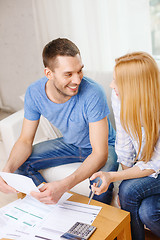 Image showing smiling couple with papers and calculator at home