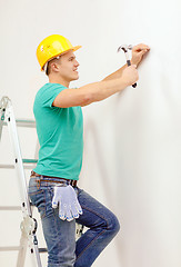 Image showing smiling man in helmet hammering nail in wall