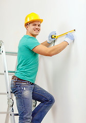 Image showing smiling man in protective helmet measuring wall