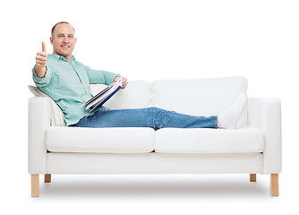 Image showing smiling man lying on sofa with book