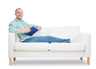 Image showing smiling man lying on sofa with book