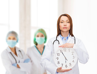 Image showing calm female doctor with wall clock