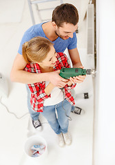 Image showing smiling couple drilling hole in wall at home