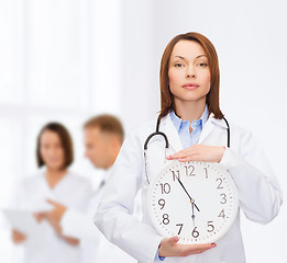 Image showing calm female doctor with wall clock