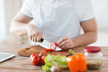 Image showing male hand cutting tomato on board with knife