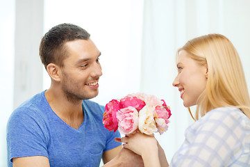 Image showing smiling man giving girfriens flowers at home