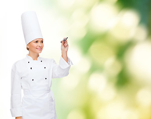 Image showing smiling female chef writing something on air