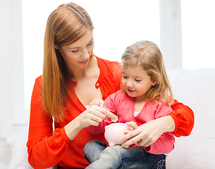Image showing happy mother and daughter with small piggy bank