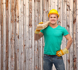 Image showing smiling manual worker in helmet with wooden boards