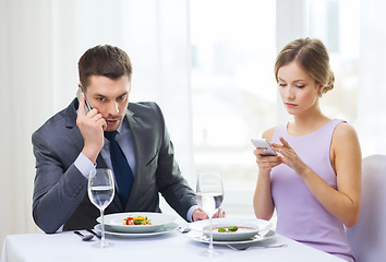 Image showing busy couple with smartphones at restaurant