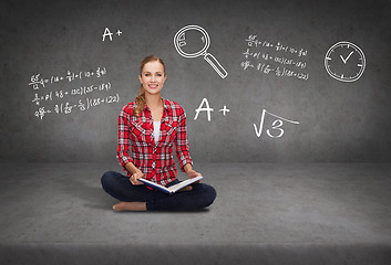 Image showing smiling young woman sittin on floor with book