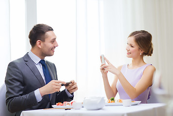 Image showing smiling couple with sushi and smartphones