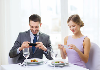 Image showing smiling couple with appetizers and smartphones