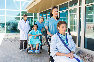 Image showing Nurses Assisting Patients On Wheelchairs Outside Hospital Buildi