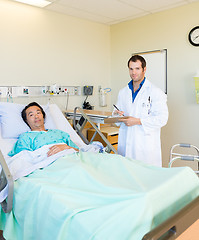 Image showing Doctor Writing On Clipboard By Patient's Bed In Hospital