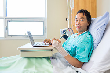 Image showing Patient With Crepe Bandage On Hand Using Laptop On Bed