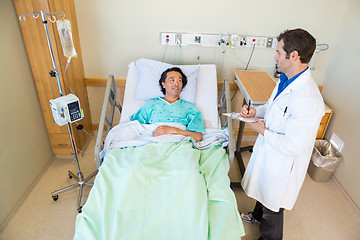 Image showing Male Doctor Looking At Patient While Writing Notes On Clipboard