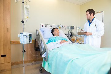 Image showing Doctor Looking At Patient While Writing Notes On Clipboard