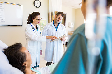 Image showing Doctors Discussing Notes With Patient And Nurse In Foreground