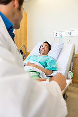 Image showing Patient Looking At Doctor Writing On Clipboard On Hospital Bed