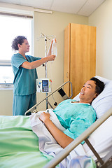 Image showing Nurse Adjusting IV Drip On Rod With Patient On Foreground