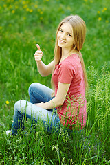 Image showing Smiling female sitting outdoors gesturing thumb up