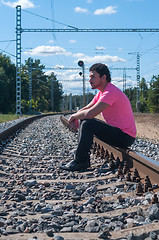 Image showing One man in pink t-shirt sitting on train tracks