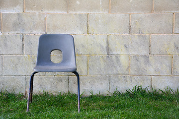Image showing Abandoned chair in front of a concrete block wall