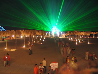 Image showing The green laser at night above a beach, people among artificial