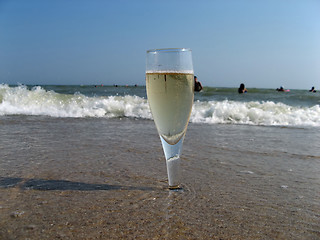 Image showing Glass of a cold champagne in warm sea waves on a beach 2