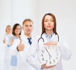 Image showing calm female doctor with wall clock