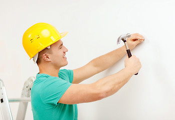 Image showing smiling man in helmet hammering nail in wall