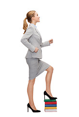 Image showing smiling businesswoman stepping on pile of books