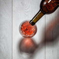 Image showing Red wine pouring into glass from bottle on white wooden table. T