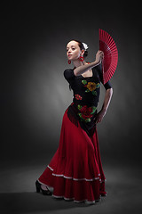 Image showing young woman dancing flamenco with fan on black