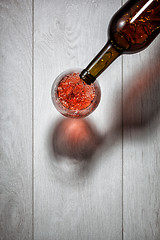 Image showing Red wine pouring into glass from bottle on white wooden table. T