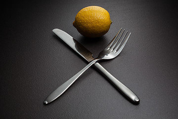 Image showing lemon with crossed knife and fork on black