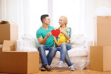 Image showing smiling couple with red heart on sofa in new home