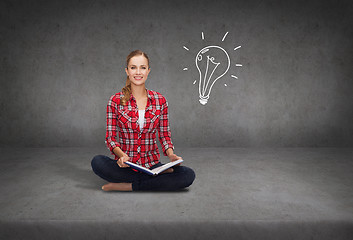 Image showing smiling young woman sittin on floor with book