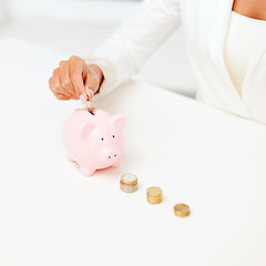 Image showing female hand putting euro coins into piggy bank