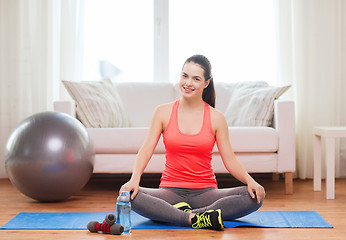 Image showing smiling girl sitting on mat with sports equipment
