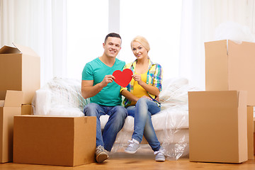 Image showing smiling couple with red heart on sofa in new home