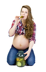 Image showing Pregnant young woman on a white background eats pickled cucumber