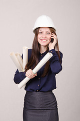 Image showing Girl a helmet talking on phone with blueprints in hand