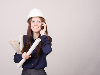 Image showing Young woman talking on phone with blueprints in hand