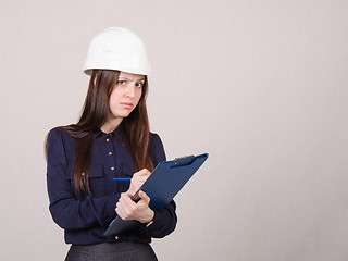 Image showing Thoughtful girl a helmet writes in pencil folder