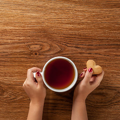 Image showing woman holding hot cup of tea with cookies