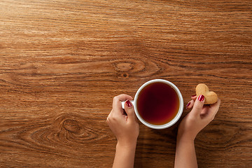 Image showing woman holding hot cup of tea with cookies