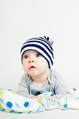 Image showing cute baby in striped hat lying down on a blanket